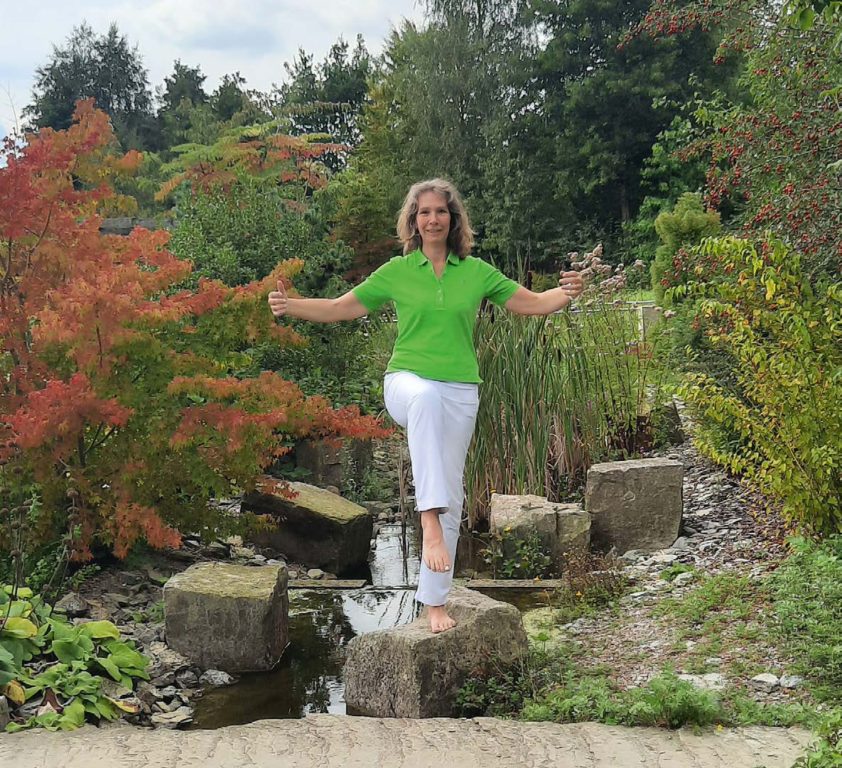 Myriam Ingenfeld balanciert im Baum-Stand auf Steinen in einem Gartenteich